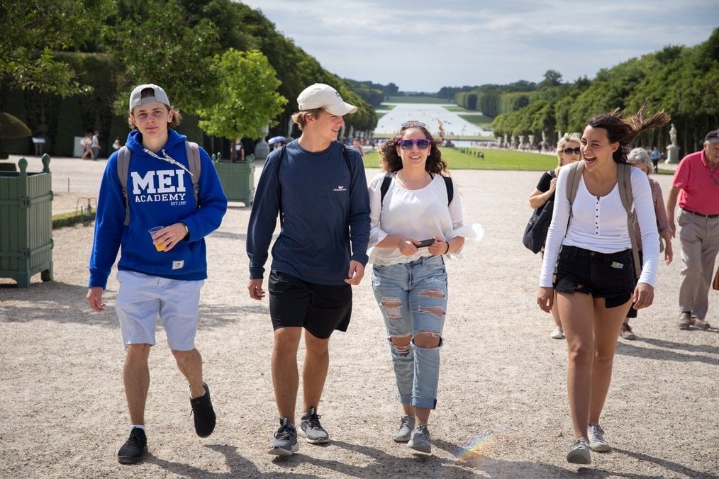 France MEI Four teens walk through a garden in France with backpacks on.